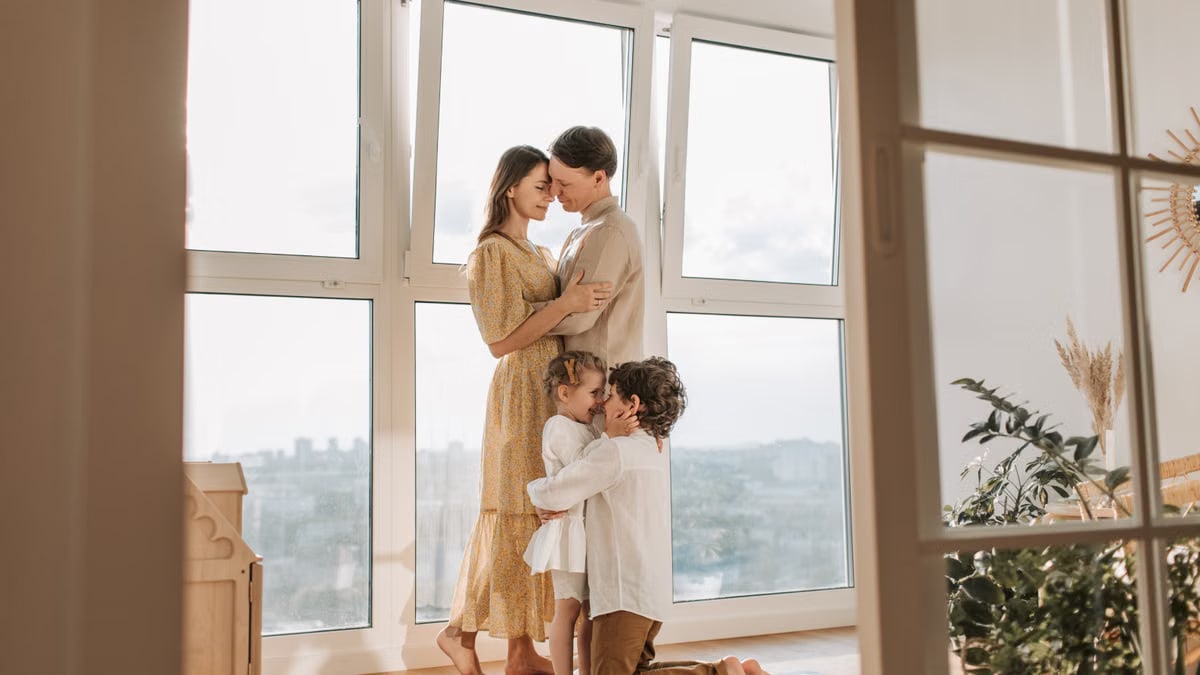 A loving family shares an affectionate moment near a bright window.